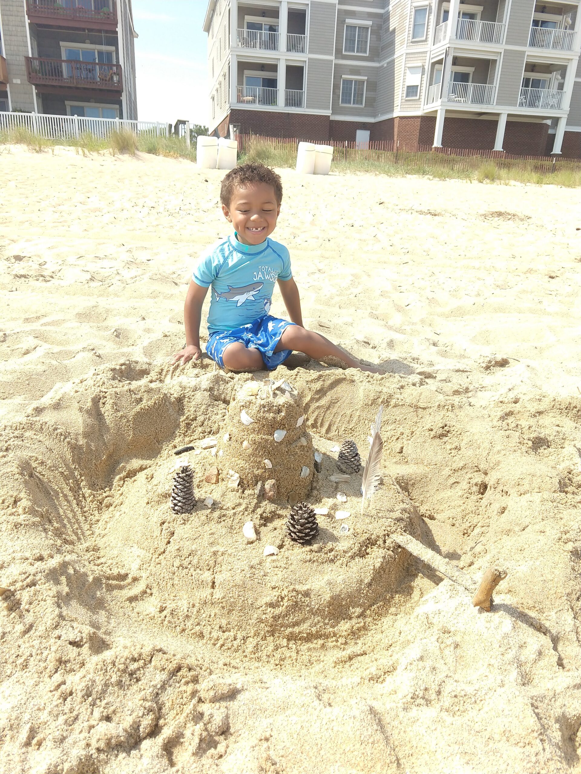 decorating the sandcastle with shells, rocks, pine cones, sticks, and feathers all found on the beach